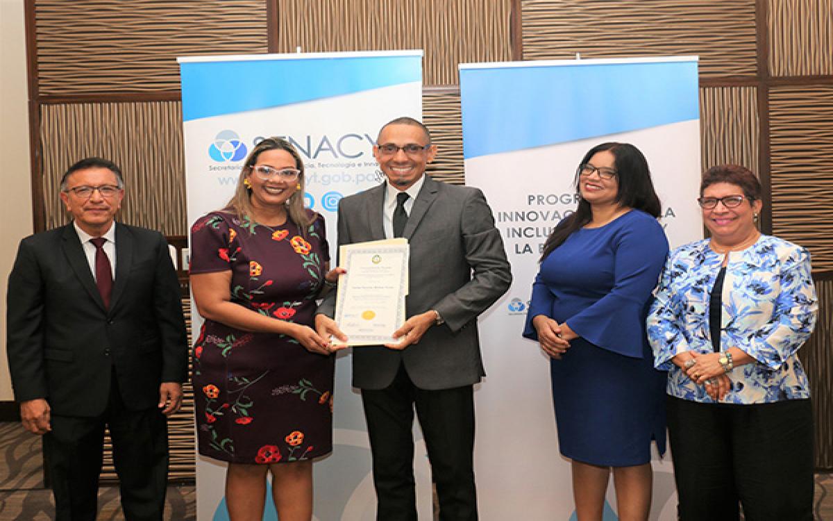 Prof. Carlos Medina, de Darien, recibe certificado por cursar diplomado de Matemáticas. Le entrega la Dra. Milena Gómez Cedeño